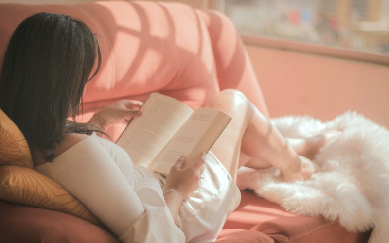 Recommended new 2022 and 2023 books on childfree living, pregnancy, parenthood and more (image: young woman reading book on cozy sofa)