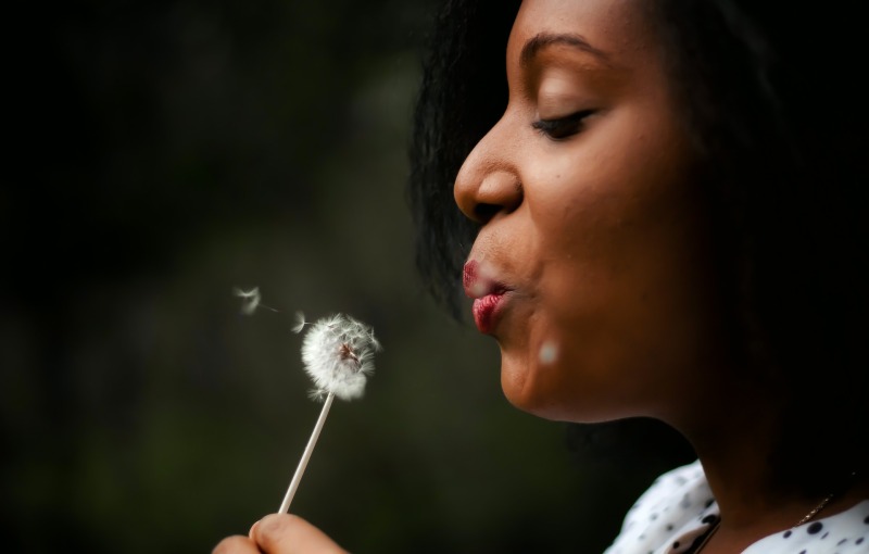 Ask Merle: Can I make the baby vs childfree decision while I'm single? And how can I be confident in my own choices? (Photo of young woman blowing on white dandelion)